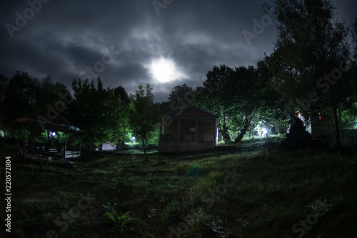 Mountain night landscape of building at forest at night with moon or vintage country house at night with clouds and stars. Summer night.