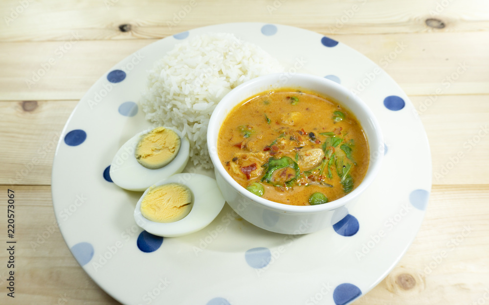 Thai Meal Kit Panang Pork Curry and boiled egg cut half in a white plate on wooden floor,Close up.