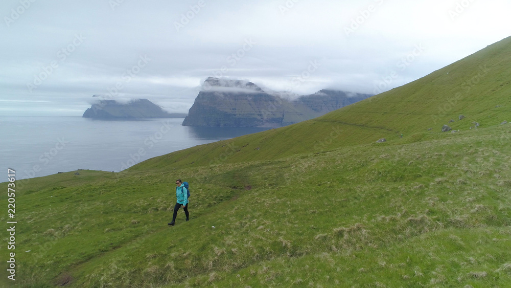 AERIAL: Hiker girl walking across a big pasture overlooking the deep blue ocean.