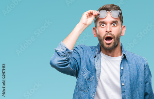 Fotografie, Obraz Young handsome man wearing sunglasses over isolated background afraid and shocked with surprise expression, fear and excited face