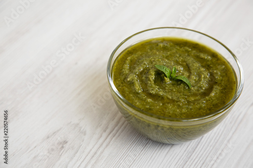 Bowl of freshly made basil pesto on white wooden surface, side view. Closeup. Copy space.