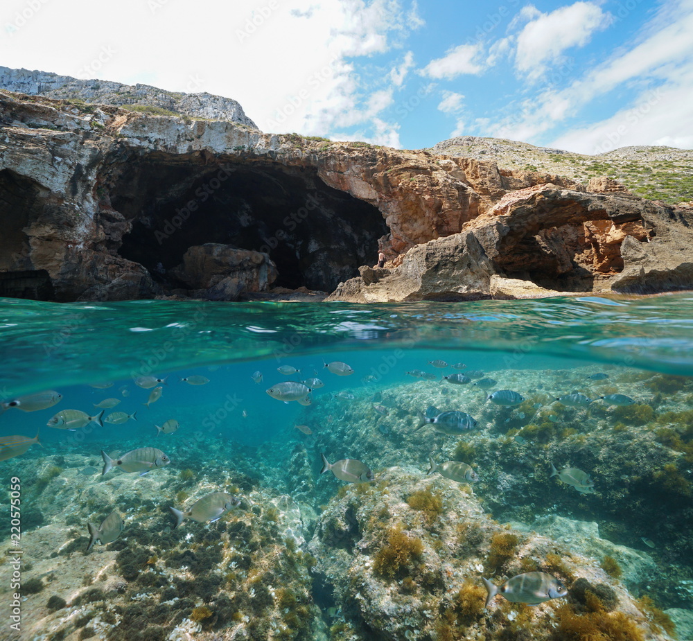 Rocky coast with large cave on the sea shore and fishes underwater, split view above and below water surface, Mediterranean, Cova Tallada, Costa Blanca, Javea, Alicante, Valencia, Spain
