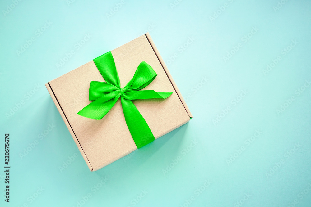 One craft paper box with green ribbon bow on blue background from above. Minimalism, copy space One craft paper box with green ribbon bow on blue background from above. Minimalism, copy space