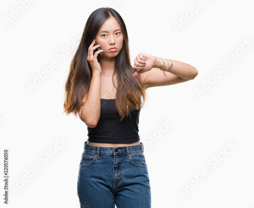 Young asian woman speaking on the phone over isolated background with angry face, negative sign showing dislike with thumbs down, rejection concept