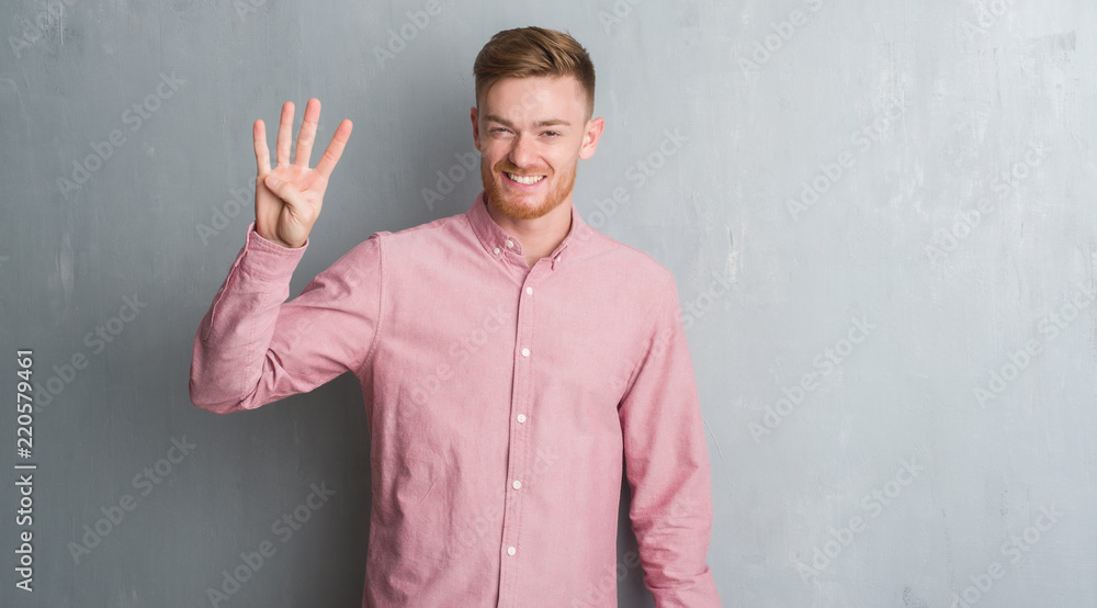 Young redhead man over grey grunge wall wearing pink shirt showing and pointing up with fingers number four while smiling confident and happy. Young redhead man over grey grunge wall wearing pink shirt showing and pointing up with fingers number four while smiling confident and happy.
