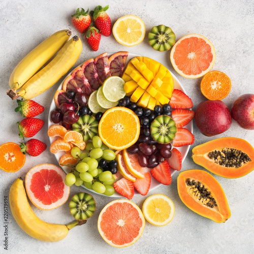 Raw fruits berries platter, mango, oranges, kiwi strawberries, blueberries grapefruit grapes, bananas apples on the white plate, on the off white table, top view, square, selective focus