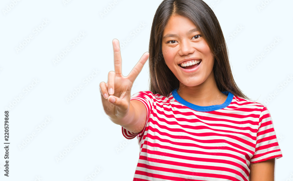 Young asian woman over isolated background smiling with happy face winking at the camera doing victory sign. Number two. Young asian woman over isolated background smiling with happy face winking at the camera doing victory sign. Number two.