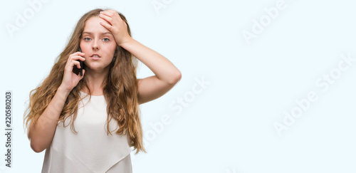 Photos Young blonde woman using smartphone stressed with hand on head, shocked with shame and surprise face, angry and frustrated