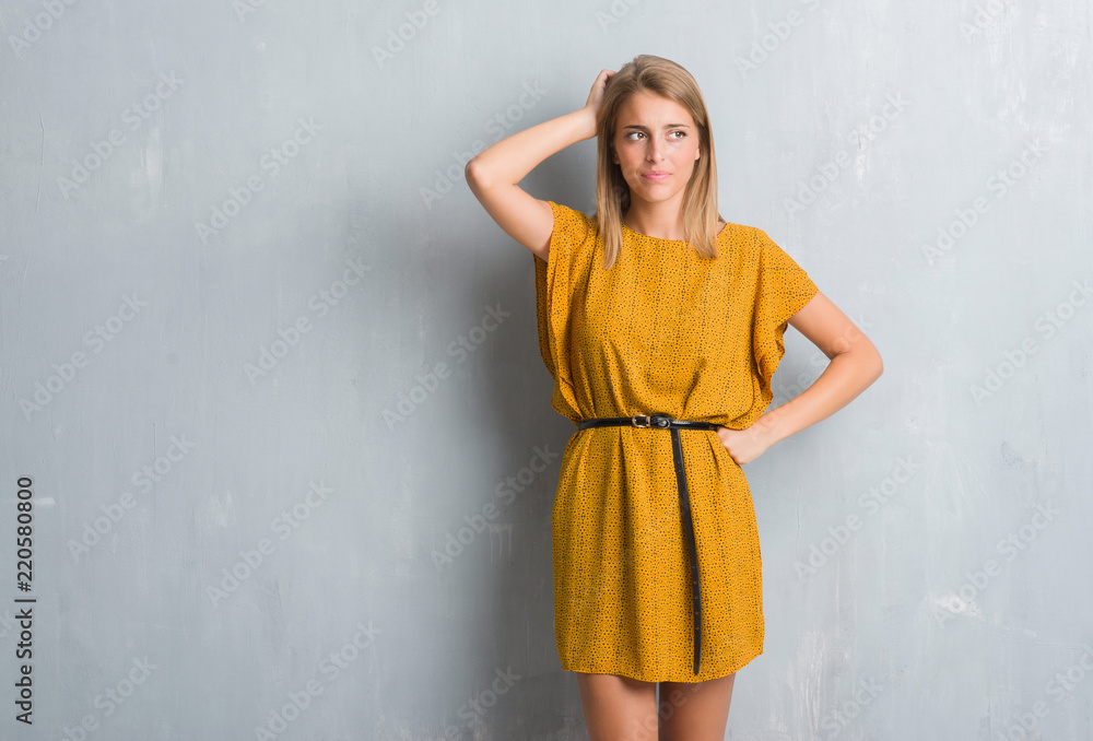 Fototapeta premium Beautiful young woman standing over grunge grey wall wearing a dress confuse and wonder about question. Uncertain with doubt, thinking with hand on head. Pensive concept.