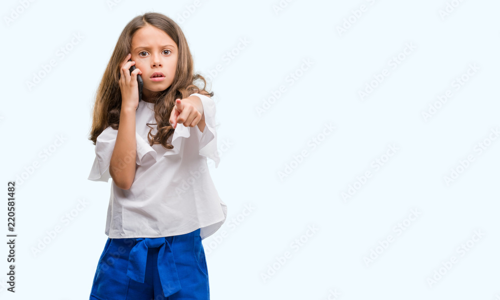 Brunette hispanic girl using smartphone pointing with finger to the camera and to you, hand sign, positive and confident gesture from the front Brunette hispanic girl using smartphone pointing with finger to the camera and to you, hand sign, positive and confident gesture from the front