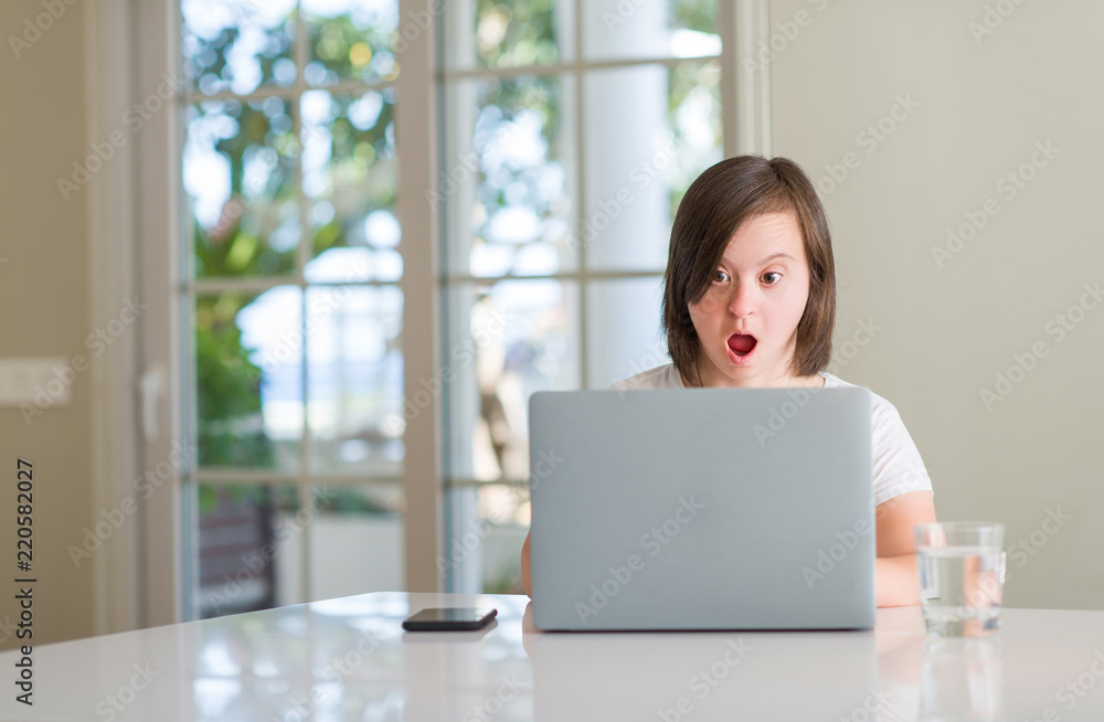Down syndrome woman at home using computer laptop scared in shock with a surprise face, afraid and excited with fear expression Down syndrome woman at home using computer laptop scared in shock with a surprise face, afraid and excited with fear expression