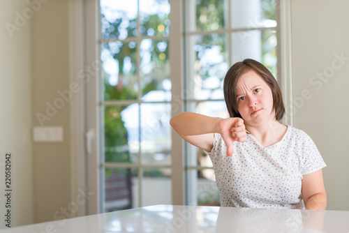Down syndrome woman at home with angry face  negative sign showing dislike with thumbs down  rejection concept