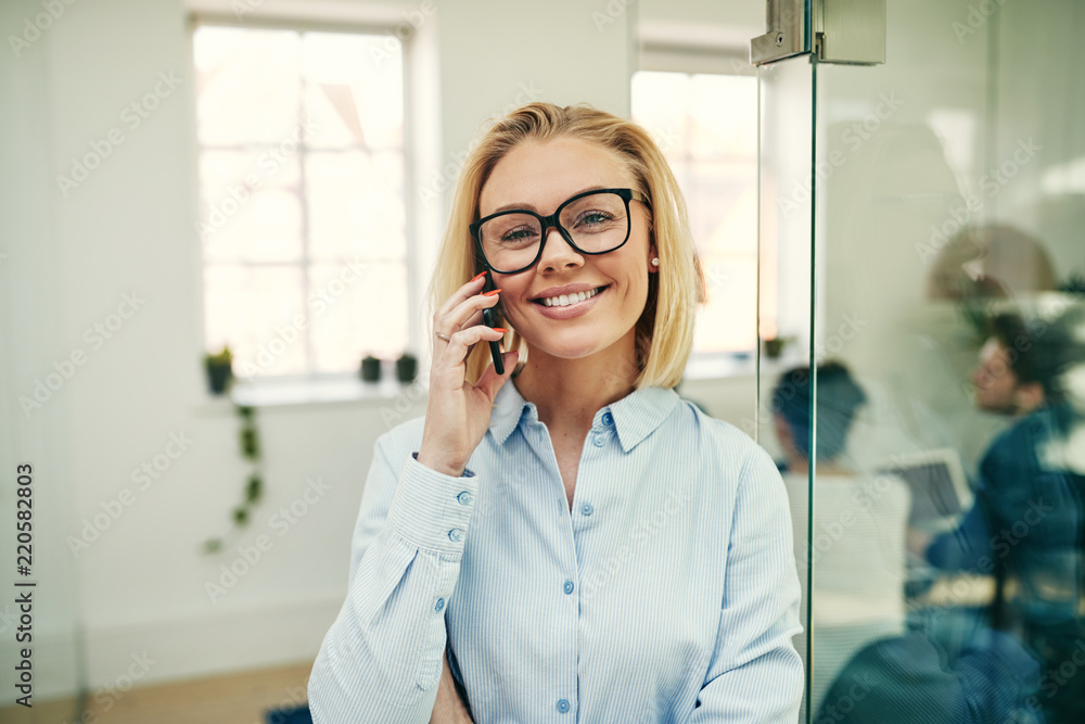 Smiling young businesswoman talking on a cellphone in an office Smiling young businesswoman talking on a cellphone in an office
