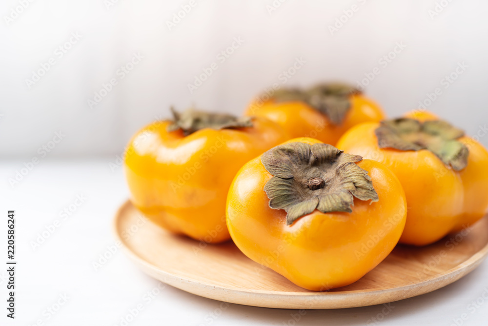 Ripe persimmon on wooden plate and white table, healthy fruit Ripe persimmon on wooden plate and white table, healthy fruit