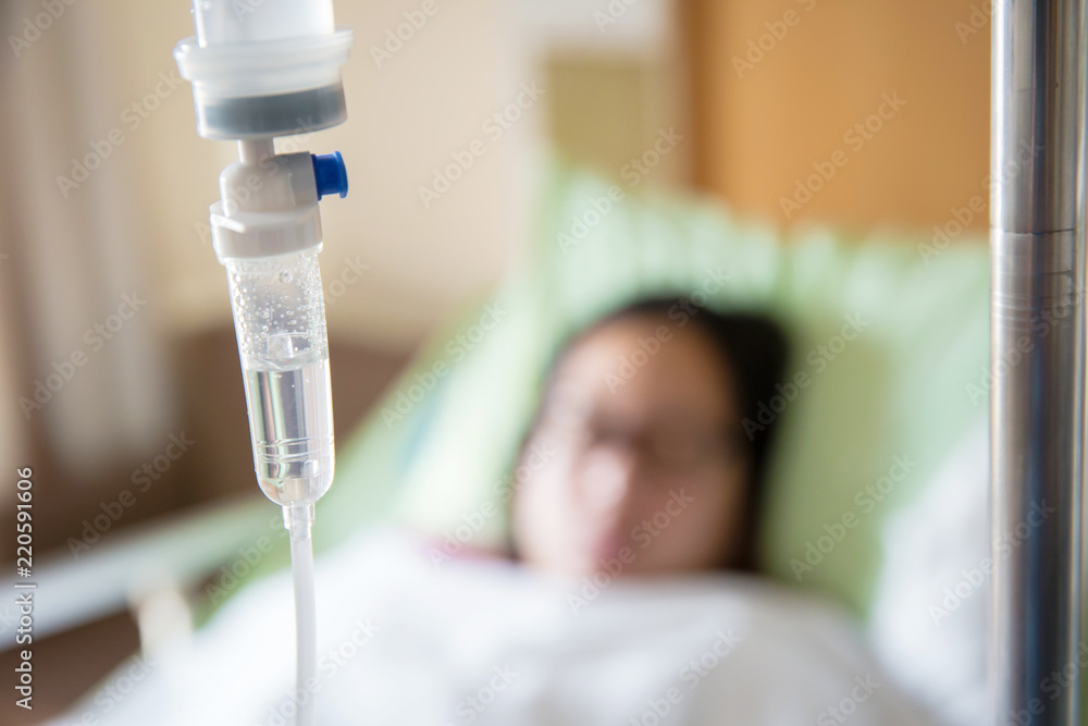 Focus the hanging saline solution with blur patient background.Illness and treatment. Health insurance. Medical Benefits. Reimbursement, Medical expenses. image for illustration, copy space, article. Focus the hanging saline solution with blur patient background.Illness and treatment. Health insurance. Medical Benefits. Reimbursement, Medical expenses. image for illustration, copy space, article.