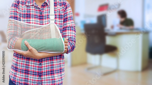 hand in a sling with broken arm in green cast isolated on blurred background working woman with office desk workplace in office