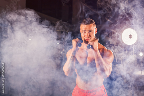 Powerful man doing boxing exercises, making direct hit with dumbbells. Photo of sporty muscular male. Strength and motivation photo