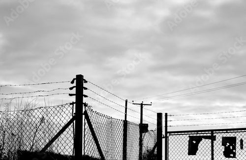 Monochrome silhouetted security fencing to farmland in rural Hampshire against an early morning cloudy sky
