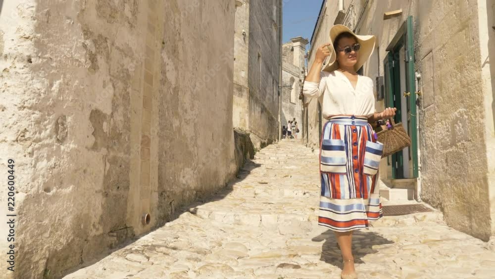 Beautiful elegant young woman walking in Matera Italy on a high balcony viewpoint with landscape. Fashion dress with hat and skirt. Beautiful elegant young woman walking in Matera Italy on a high balcony viewpoint with landscape. Fashion dress with hat and skirt.