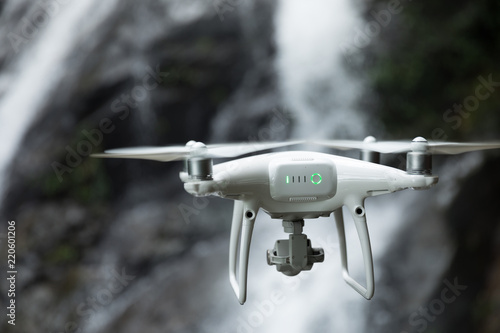 White drone with camera flying taking photo of waterfall