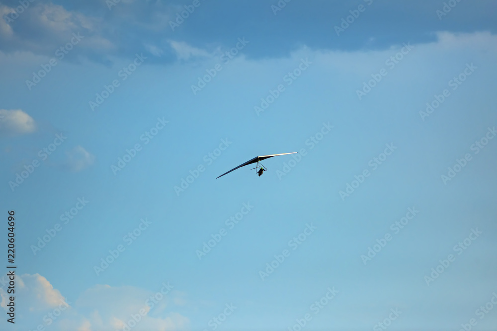 Silhouette of hang glider against blue sky with thunderclouds. Copy space.