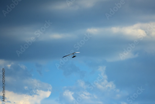 Silhouette of hang glider against blue sky with thunderclouds. Copy space.