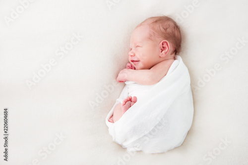 Smiling newborn baby sleeps swaddled in a white diaper