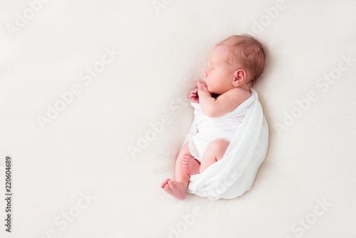 Cute newborn baby lies swaddled in a white blanket. Copy space and top view