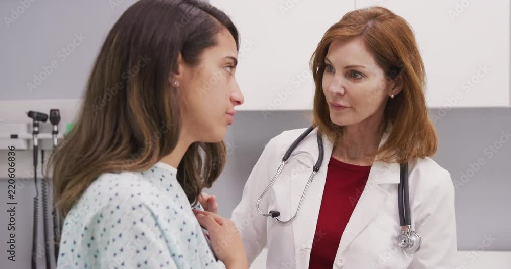Professional female doctor attending to young latina patient in hospital gown Professional female doctor attending to young latina patient in hospital gown