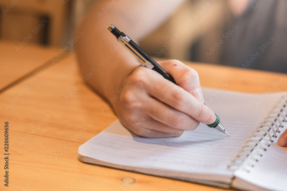 Woman hand writing in notebook on wooden table Woman hand writing in notebook on wooden table