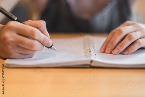 Woman hand writing in notebook on wooden table