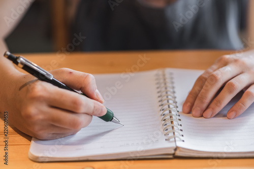 Woman hand writing in notebook on wooden table