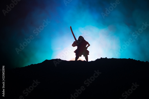 Fighter with a sword silhouette a sky ninja. Samurai on top of mountain with dark toned foggy background.