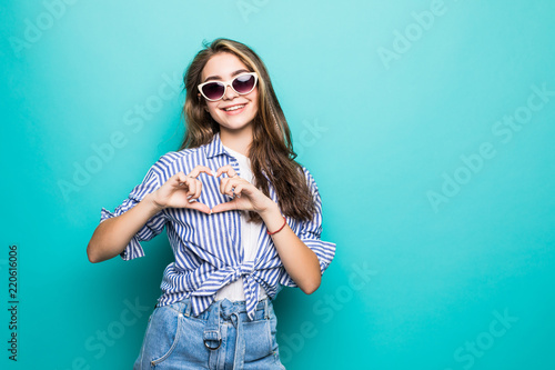 Cheerful young beautiful woman is gesturing a heart with fingers on blue background © F8  \ Suport Ukraine