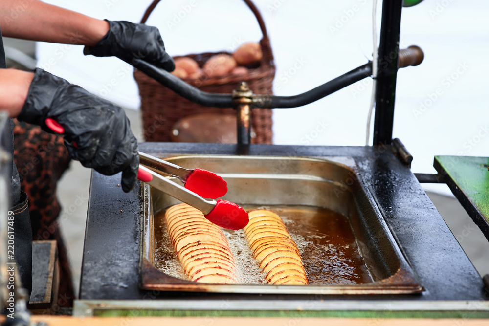 Chef cooking in a deep fryer twisted potatoes on wooden sticks. Gloved hand  lowers potatoes into