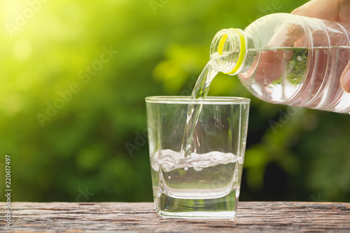 Female hand pouring water from bottle to glass on nature background.