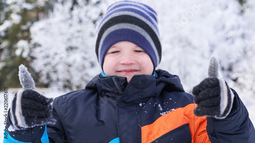Cute Caucasian boy giving thumbs up, playing and laughing on snowy winter walk in nature. Frost winter season.
