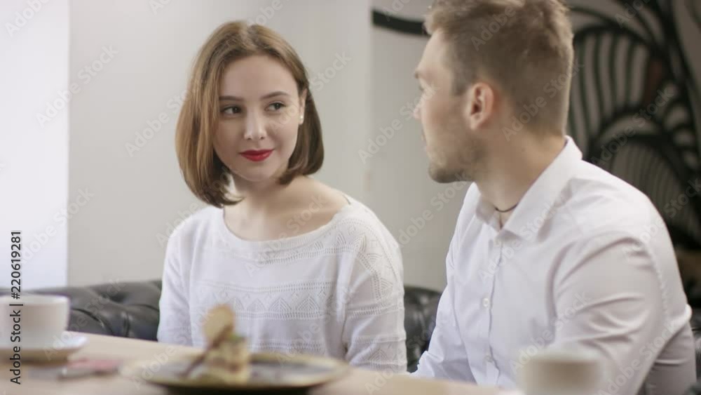 Two young зущзду are sitting in a cafe. They are sitting in the cafe at the table during coffee break. They are talking and drinking coffee. man pays the reckoning by electronic contactless payment Two young зущзду are sitting in a cafe. They are sitting in the cafe at the table during coffee break. They are talking and drinking coffee. man pays the reckoning by electronic contactless payment