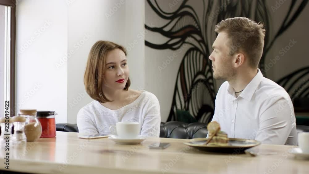 Two young people is sitting in a cafe. Man and woman are smiling and ...