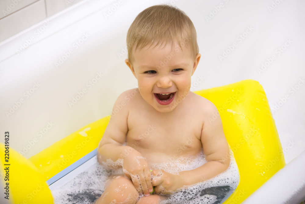Smiling baby having fun bathing with toys and foam in bathtub, excited little kid enjoying taking bath in washroom, happy adorable child playing and laughing in yellow rubber boat in bathroom Smiling baby having fun bathing with toys and foam in bathtub, excited little kid enjoying taking bath in washroom, happy adorable child playing and laughing in yellow rubber boat in bathroom