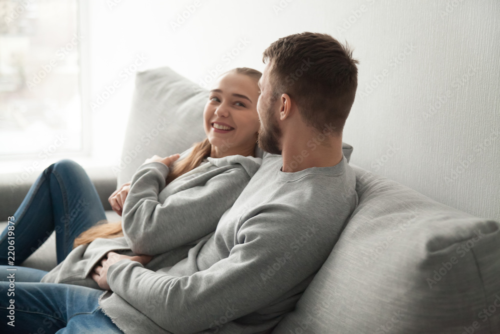 Loving young couple hugging relaxing on cozy sofa at home, smiling boyfriend and girlfriend looking in eyes enjoying each other company resting on couch, lovers embrace spending time together at home Loving young couple hugging relaxing on cozy sofa at home, smiling boyfriend and girlfriend looking in eyes enjoying each other company resting on couch, lovers embrace spending time together at home