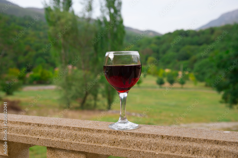 Outdoor picnic setting with wine or glass of wine on balcony with green field and mountains on background