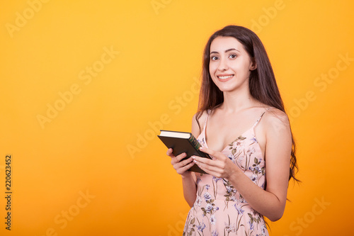 Gorgeous young woman holdin a book in studio over yellow background.