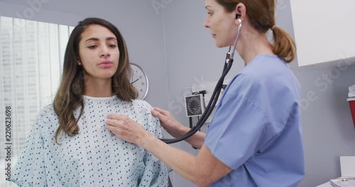 Mid aged nurse using stethoscope to examine young patients lungs and heart