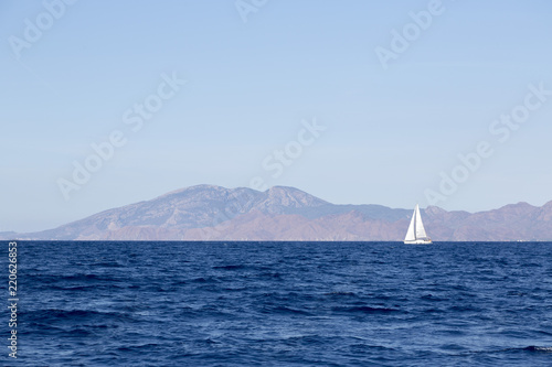 Sailing boat cruising in blue waters, mountains and shore seeing in background