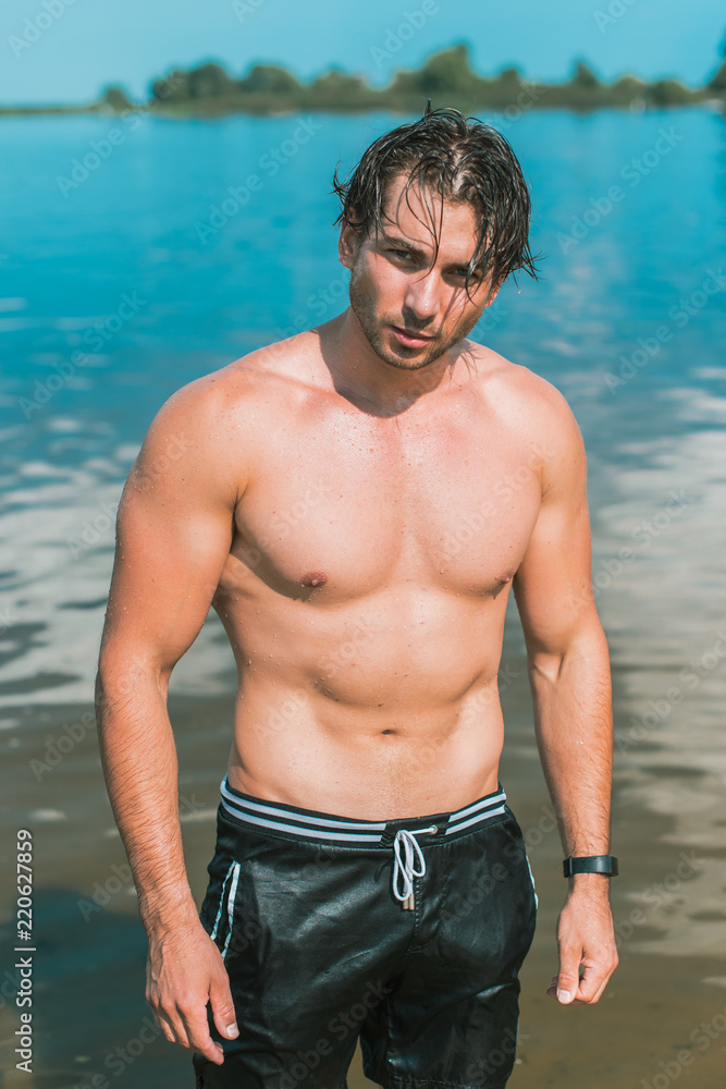 Muscular young athletic sexy man on the beach with a fit torso. Strong and handsome. Portrait of young european man on the sea beach. 