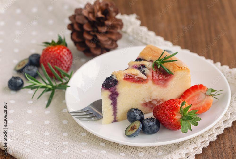 Mixed berry butter cake with fresh blueberries and strawberries on white plate put on wood table in side view copy space. Delicious and moist with sweet and sour taste in homemade bakery concept. Mixed berry butter cake with fresh blueberries and strawberries on white plate put on wood table in side view copy space. Delicious and moist with sweet and sour taste in homemade bakery concept.
