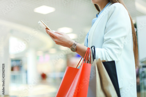 Woman using smartphone and holding shopping bag while standing on the mall background.