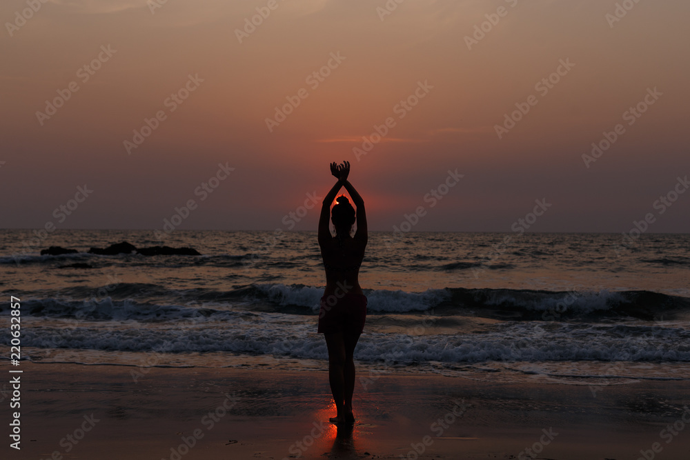 A girl is enjoying the sunset on the ocean. Hands are raised and connected together. Natural backlight.