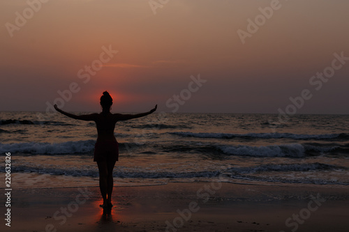 A young slender woman with a beautiful back body is engaged in yoga at sunset on the beach.Natural backlight.